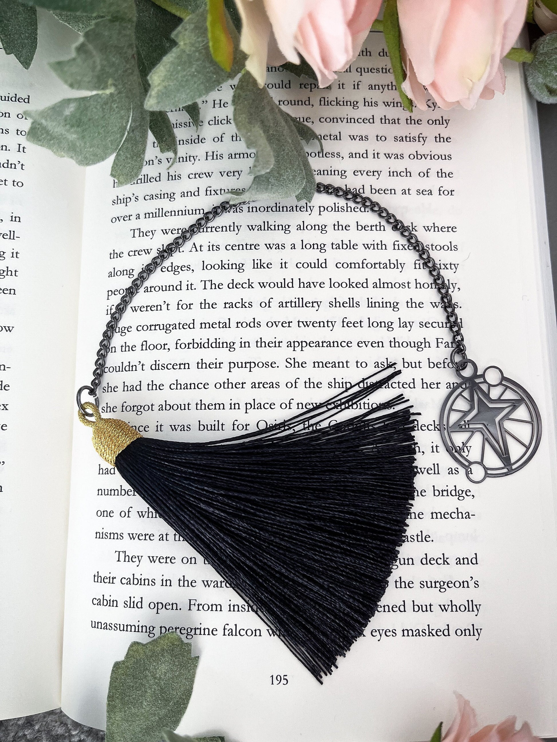 a small black metal artdeco style star bookmark attached to a chain, attached to a satin black tassel with a shiny gold top.