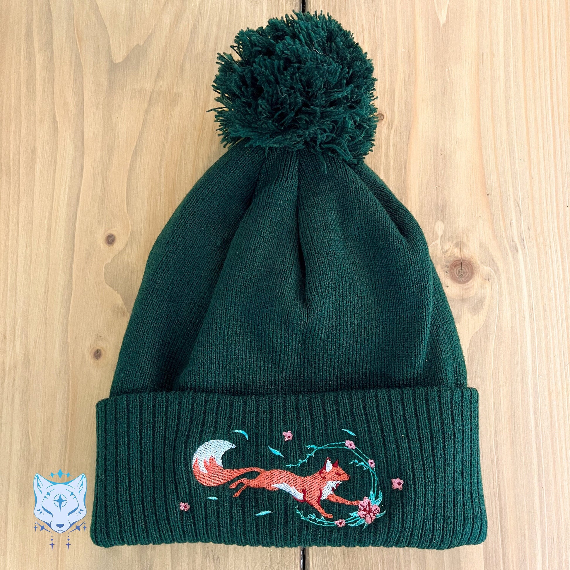 a red fox running in spring flowers and leaves, on a bottle green beanie with a pom pom